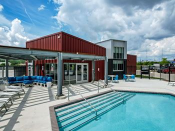 A swimming pool area with a red building and blue seating.at Linc, Des Moines  